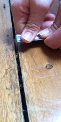 A floorboard gap being cleaned with a metal bracket