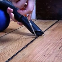A floorboard gap bein gcleaned with a screwdriver and a hoover