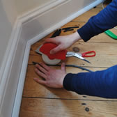 DraughtEx being fitted in a gap between two floorboards